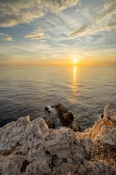 Sunset over calm ocean waters near rocky coastline Stock Photos