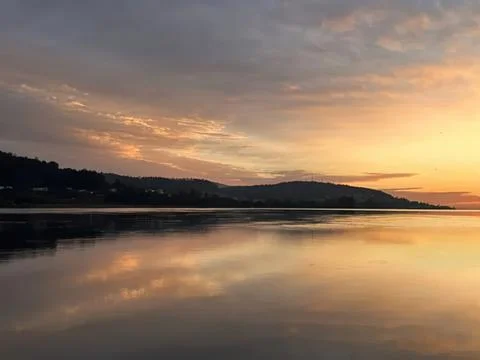Sunset over calm river with distant hills and cloudy sky Stock Photos