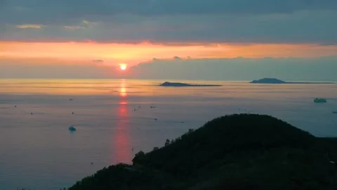 Sunset over calm sea with distant islands and fishing boats seen from coastal Видео 348545356