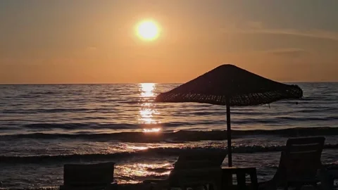 Sunset over calm sea with empty beach chairs and umbrella silhouette  Stock-Footage 337402193