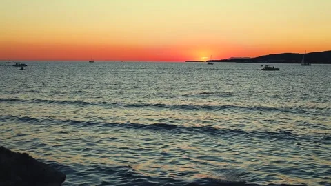Sunset over calm sea with silhouetted boats and distant hills Stock-Footage 344813373