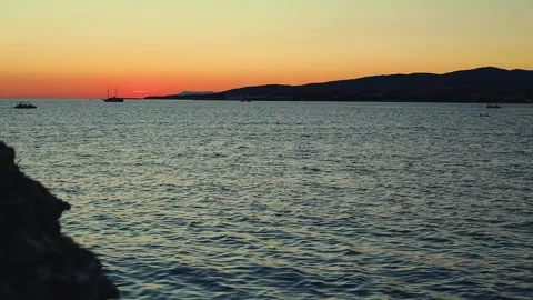 Sunset over calm sea with silhouetted boats and distant hills Stock-Footage 344813540