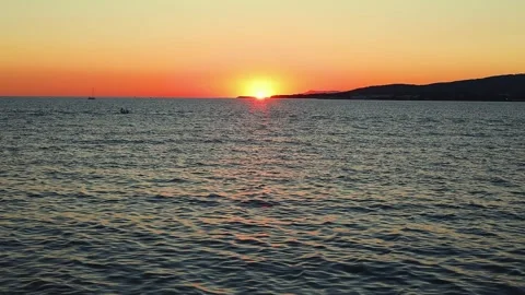 Sunset over calm sea waters with boats visible on the horizon, Stock Footage 344813367