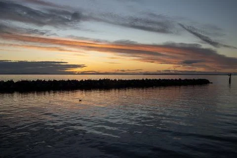 Sunset over calm water with clouds reflecting vibrant colors at a coastal l.. Stock Photos