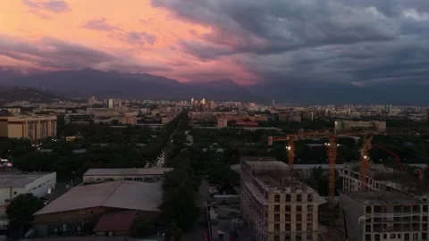 Sunset over city skyline with construction cranes and mountains in background Stock Footage 339124107