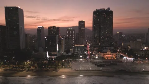 Sunset over the city skyline with lights illuminating the beach and buildings Stock Footage 297929133