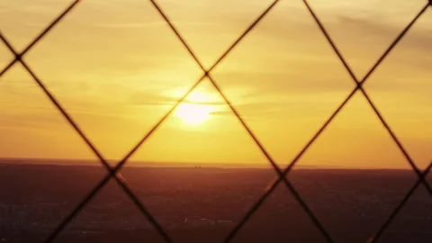 Sunset over a city viewed through a wire fence grid, with vivid golden skies. Vídeos de archivo 314085245