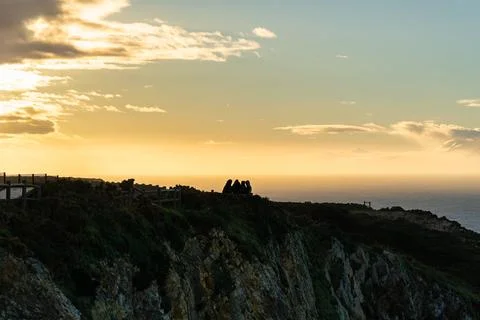 Sunset over the cliffs on the seashore with a group of people in silhouette Stock Photos