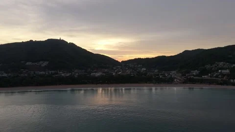 Sunset over coastal town with mountains reflecting on calm water surface Vídeos de archivo 337417800