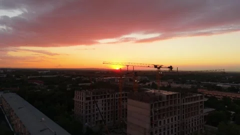 Sunset over construction site with cranes and buildings silhouetted against sky Stock Footage 339123946