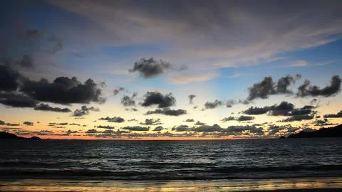 Sunset over dark ocean with cloudy sky and distant horizon Stock Photos