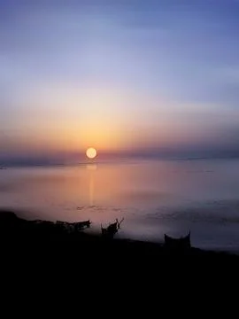 Sunset over the evening sky at the beach with boats in the river water, Ilustração Stock