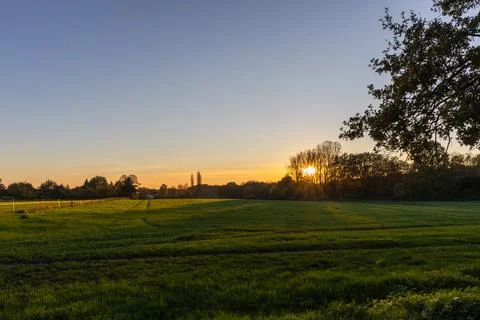 Sunset over a field with trees in the foreground and a church in the background Stock Photos