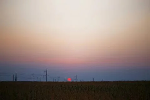 Sunset over flat field with power lines and colorful sky Stock Photos