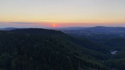 Sunset over forested hills and valley with distant village, wind turbines on Stock Footage 345170832