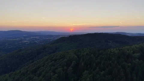 Sunset over forested mountains reveals distant valley town under peach pink blue Stock Footage 345170923