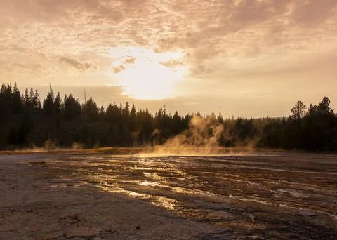 Sunset over geothermal features with steaming ground and forest backdrop in.. Stock Photos