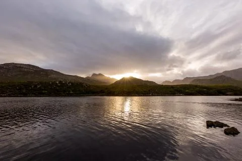 Sunset over golden lake with dramatic clouds and mountain range Stock Photos