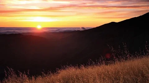 Sunset over grassy hillside and above clouds Stock-Footage 76760503