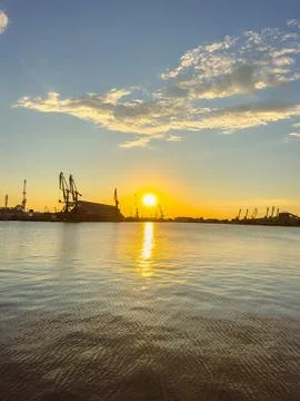 Sunset over a harbor with cranes and water reflections Stock Photos