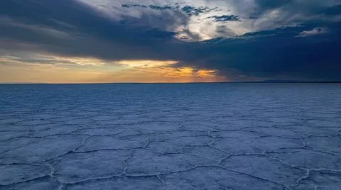 Sunset over icy salt flat with dark clouds and bright sky Stock Photos
