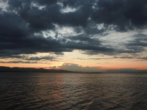 Sunset over the lake with dramatic clouds and mountains in the background Stock Photos