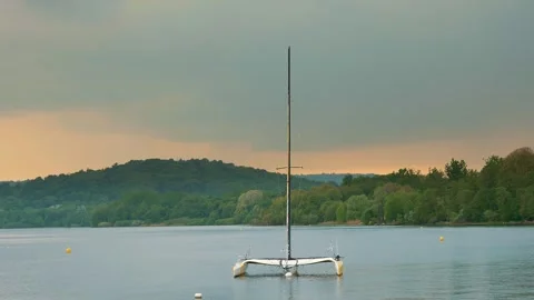 Sunset over lake. lone sailing boat, catamaran, moored in the bay of the lake Stock Footage 252426417