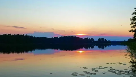 Sunset over lake with trees and calm water reflecting colors in evening sky Stock Footage 327181579