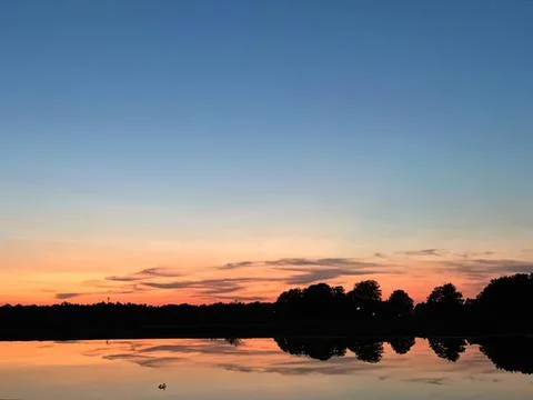 Sunset over lake with trees and calm water reflection Stock Photos