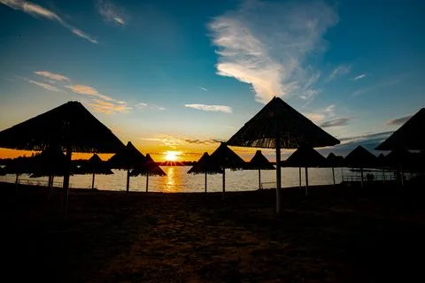Sunset over lake view over thatched beach umbrella, wooden sunshade Stock Photos