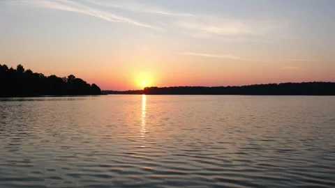 Sunset over lake water with trees on horizon. Sun setting on lake surface in Vidéo 340356844