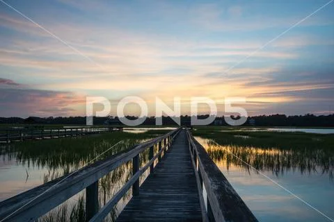 Sunset over a long boardwalk over an ocean marsh at high tide Stock Photos