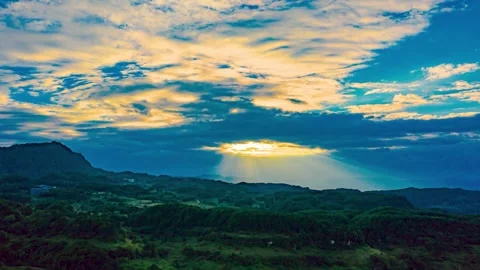 Sunset over lush green mountains with sun rays piercing through clouds Stock Footage 342091099