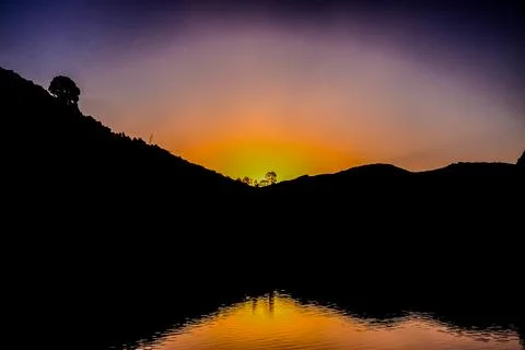 A sunset over a mountain range with a tree in the foreground Stock Photos