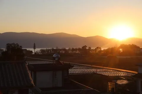 Sunset over mountain silhouettes, fields, and dark rooftops 库存照片