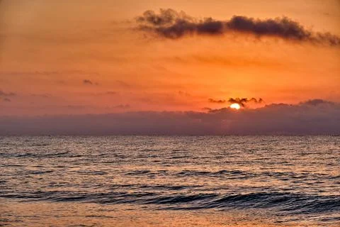 Sunset over ocean with calm waves and distant clouds reflecting warm colors.. Stock Photos