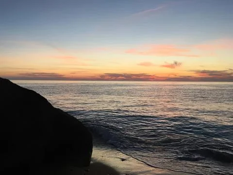 Sunset over the ocean with calm waves and rocky shore Stock Photos