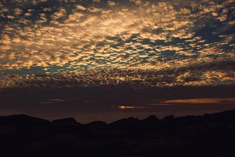 Sunset over ocean with clouds and rocky shore viewed from coastal area in eve Stock Photos