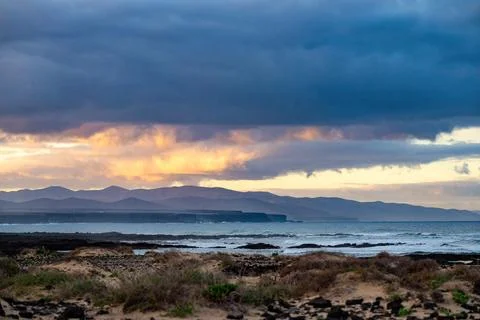 Sunset over the ocean with clouds and mountains in the background Stock Photos