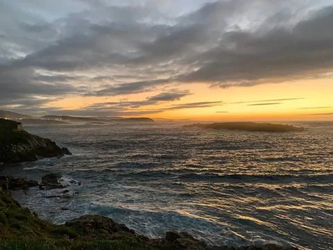 Sunset over ocean with cloudy sky and rocky shore Stock Photos