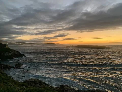 Sunset over ocean with cloudy sky and rocky shoreline Stock Photos