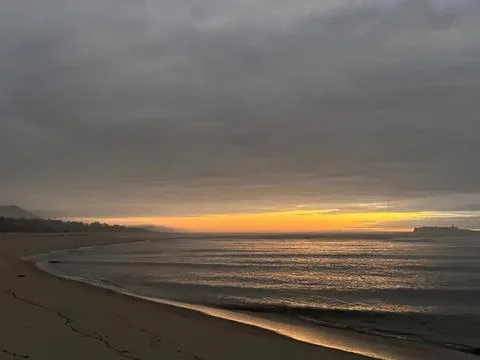 Sunset over the ocean with cloudy sky and sandy beach Stock Photos