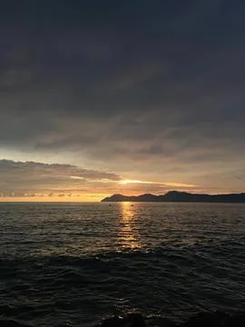 Sunset over the ocean with dark clouds and distant land Stock Photos