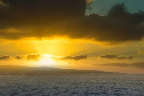 Sunset over ocean with dark clouds and golden sky Stock Photos