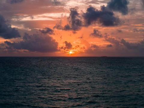 Sunset over ocean with distant atoll silhouette and glowing clouds Stock-Fotos