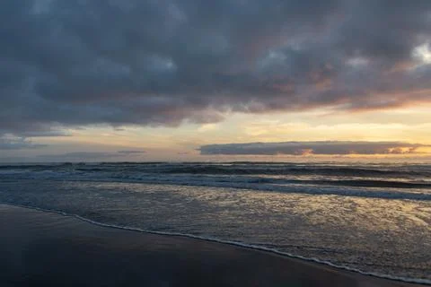 Sunset over the ocean with gentle waves and cloudy sky at a serene beach lo.. Stock Photos
