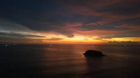 Sunset over ocean with island silhouette and distant boats illuminated Видео 340407343
