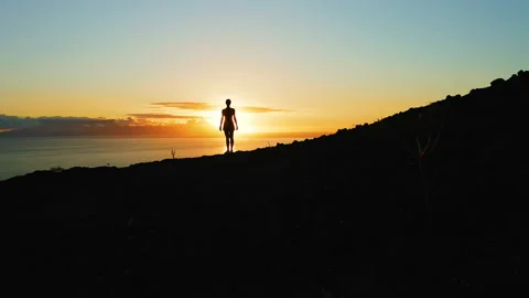 Sunset over ocean with mountain landscape. Lonely woman silhouette. Aerial of Video stock 232724633