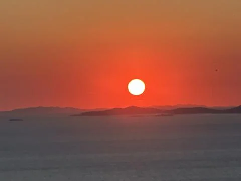 Sunset over the ocean with red and orange sky, viewed from a hilltop near the Fotos Stock
