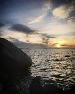 Sunset over ocean with rocks and cloudy sky Stock Photos
